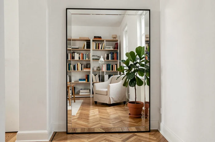 Grand miroir surdimensionné appuyé contre le mur d'une pièce étroite reflétant le salon pour créer une illusion d'espace et de profondeur